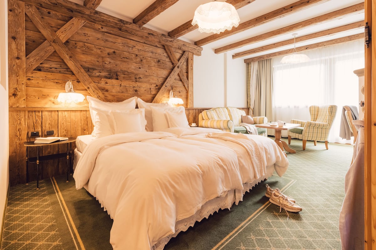 A cozy bedroom with a large bed, a small table, a chair, and a window with curtains.