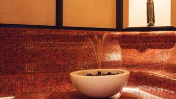 A spa area with a mosaic-tiled bench, a white bowl with black stones, and a statue on a wall.