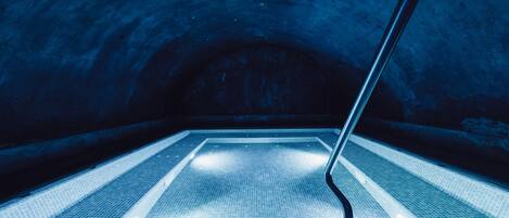 A tiled pool with a metal handrail, surrounded by a dark, arched ceiling.
