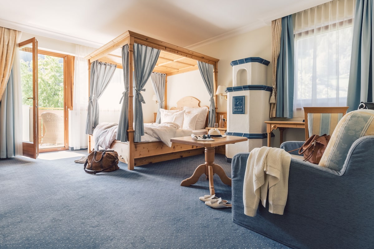 A bedroom with a four-poster bed, a sofa, a small table, and a view of the outdoors.