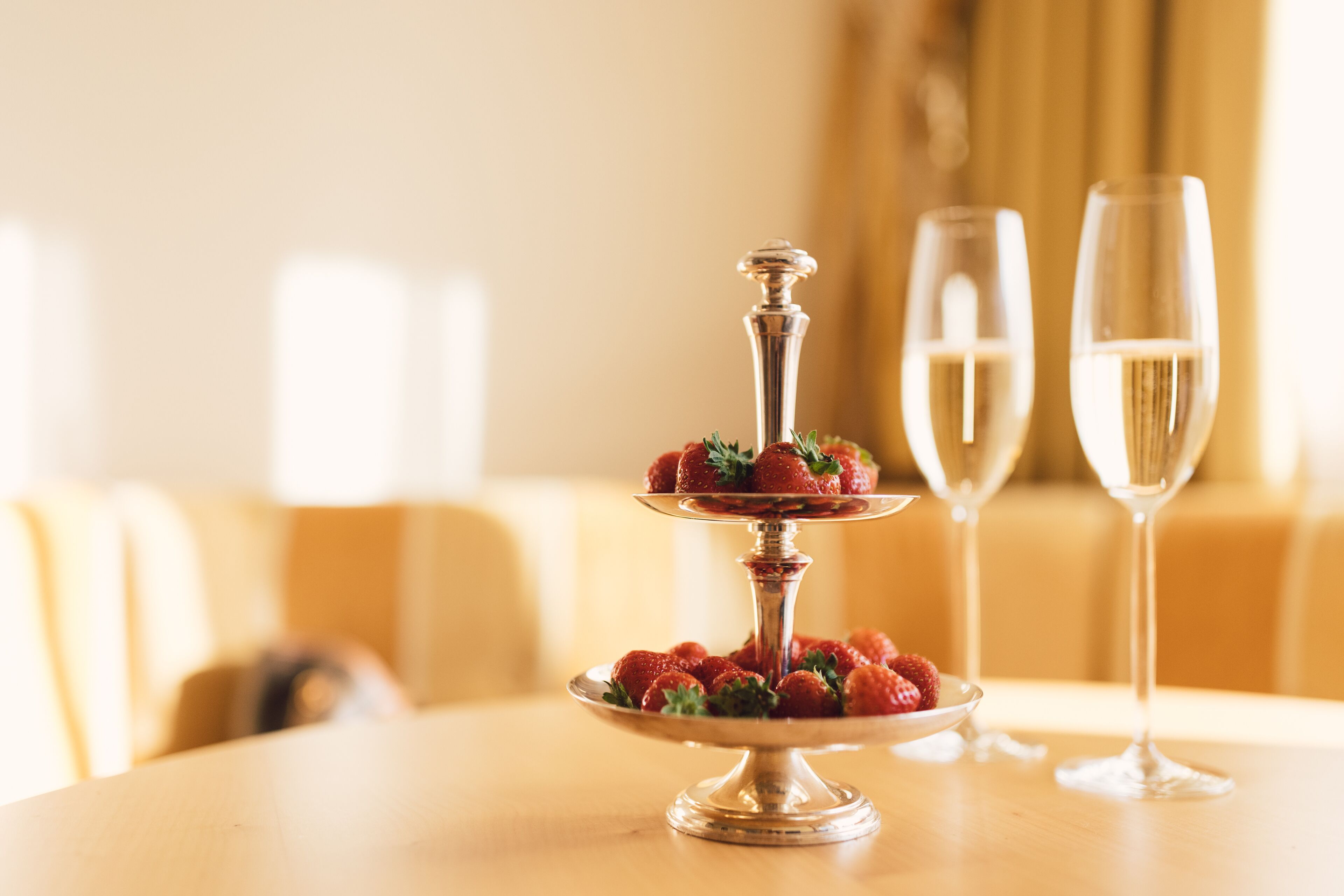 Un elegante expositor plateado de tres niveles con fresas sobre una mesa, junto con dos copas de champán.
