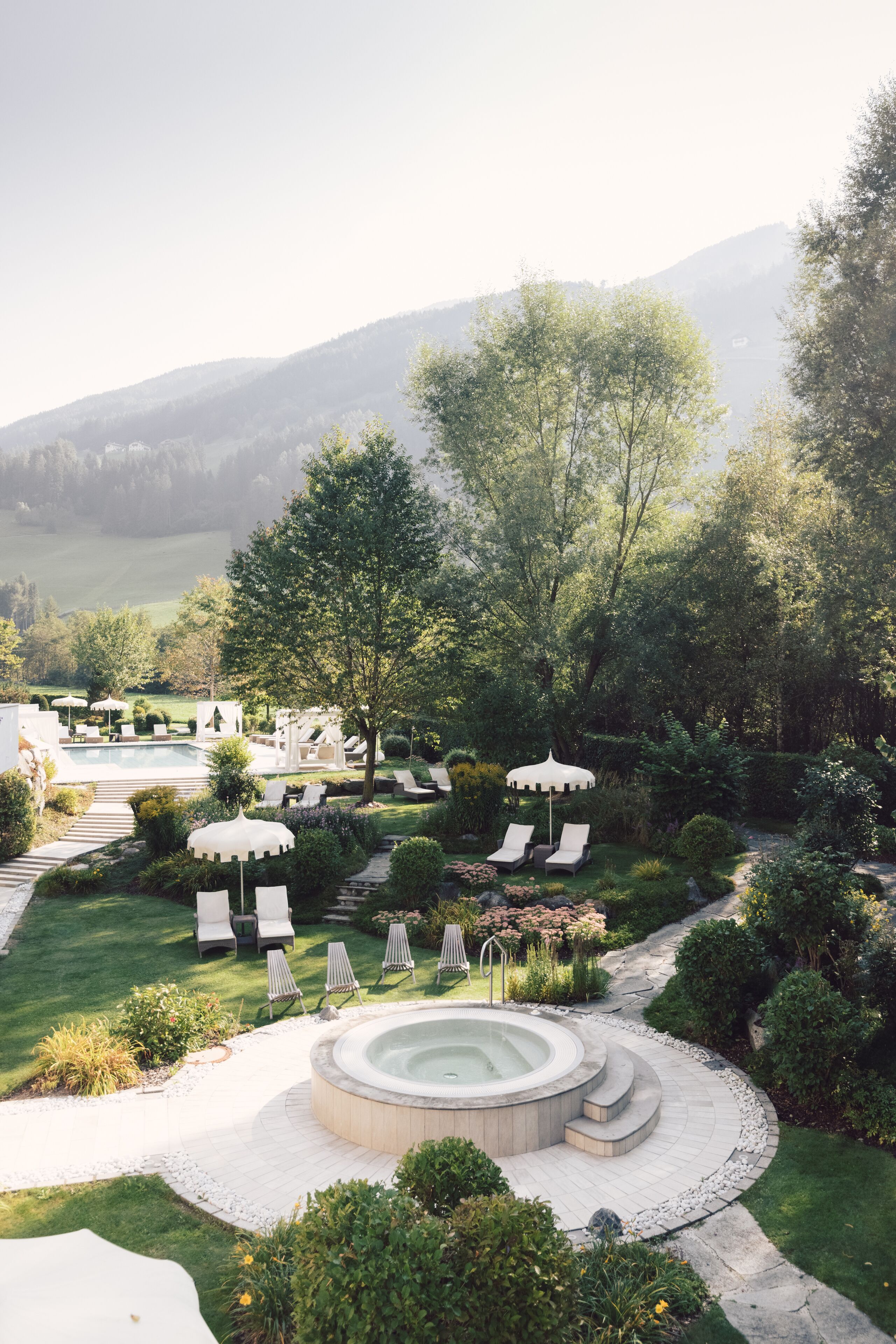 A landscaped garden with a hot tub, lounge chairs, and umbrellas.