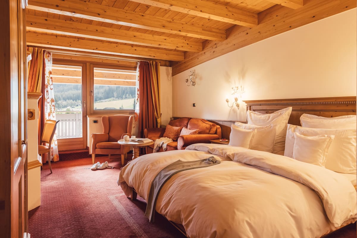 A hotel room with a large bed, a wooden ceiling, a view of the outdoors, a chair, and a small table.