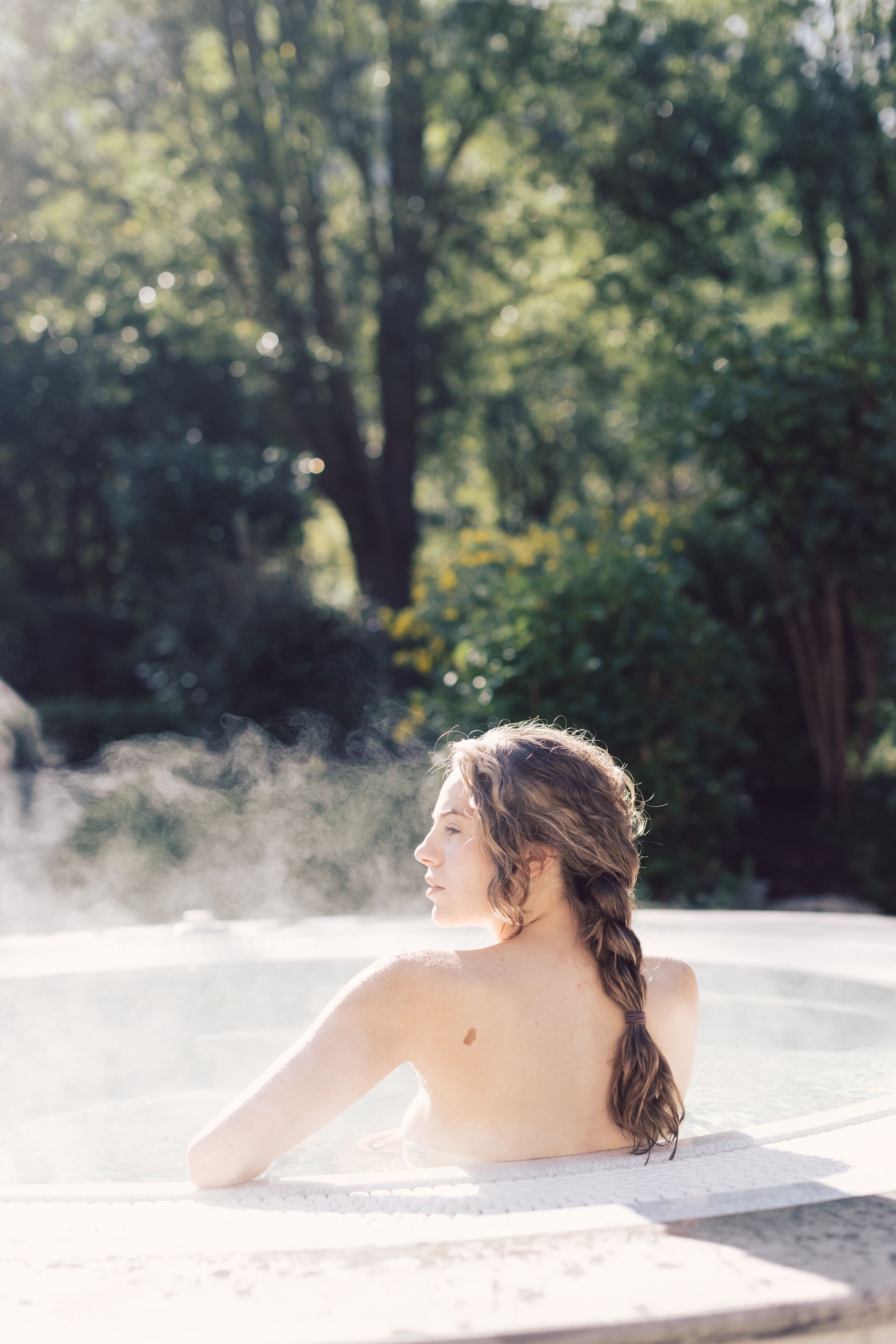 A person relaxing in a hot tub surrounded by greenery.