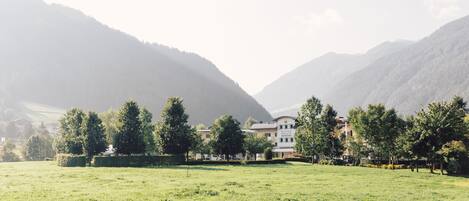 A hotel with a large building surrounded by lush green fields and mountains in the background.