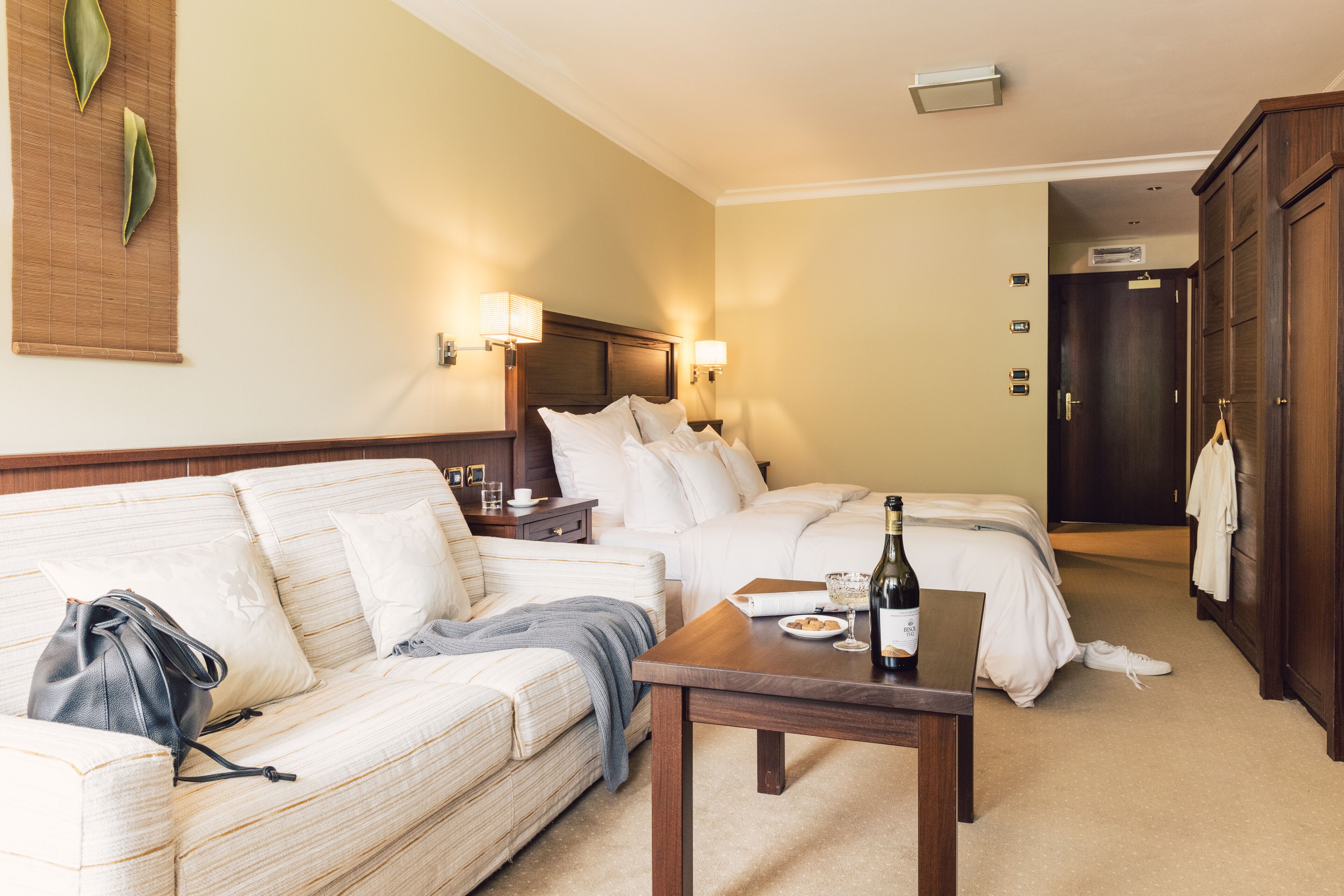 Ein Hotelzimmer mit Bett, Sofa, Tisch mit Flasche und Teller, Lampe und Kleiderschrank.
