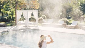 A woman in a white dress sitting by a pool with a gazebo and lounge chairs in the background. - Alpenpalace Luxury Hideaway & Spa Retreat (Valle Aurina)