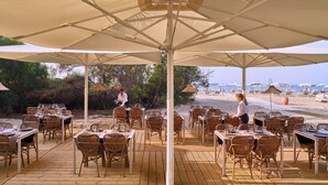 An outdoor dining area with tables and chairs, umbrellas, and a view of the beach and ocean. - Serenè Resort (Cutro)