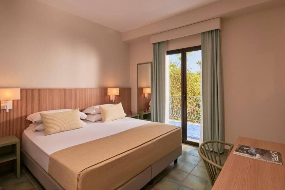 A hotel room with a bed, bedside tables, a desk, and a balcony with curtains.
