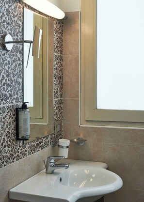 A bathroom with a white sink, a mirror with a light, and a window. -  Serena Majestic Hotel (Montesilvano)