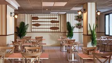 Un restaurante con sillas y mesas de madera, paredes a rayas y plantas en macetas.