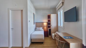 Una habitación de hotel pequeña con cama, mesita de noche, escritorio, silla y televisor montado en la pared.