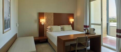 Een hotelkamer met een bed, nachtkastje, stoel en uitzicht op de omgeving door een groot raam.