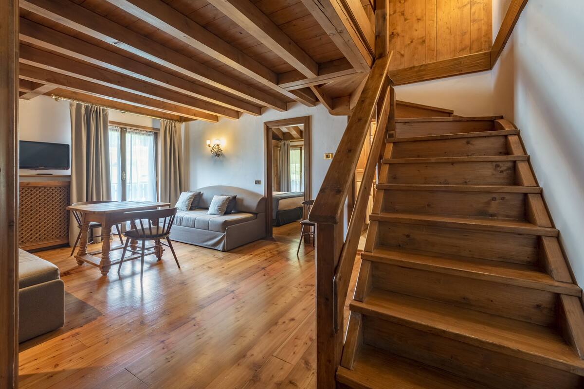 A wooden staircase leading to an upper level, a wooden dining table with chairs, a sofa, and a television on a stand.