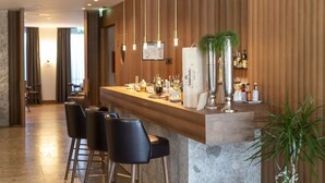 Un espace bar moderne avec un comptoir en bois, des tabourets de bar, des luminaires suspendus et une plante en pot.