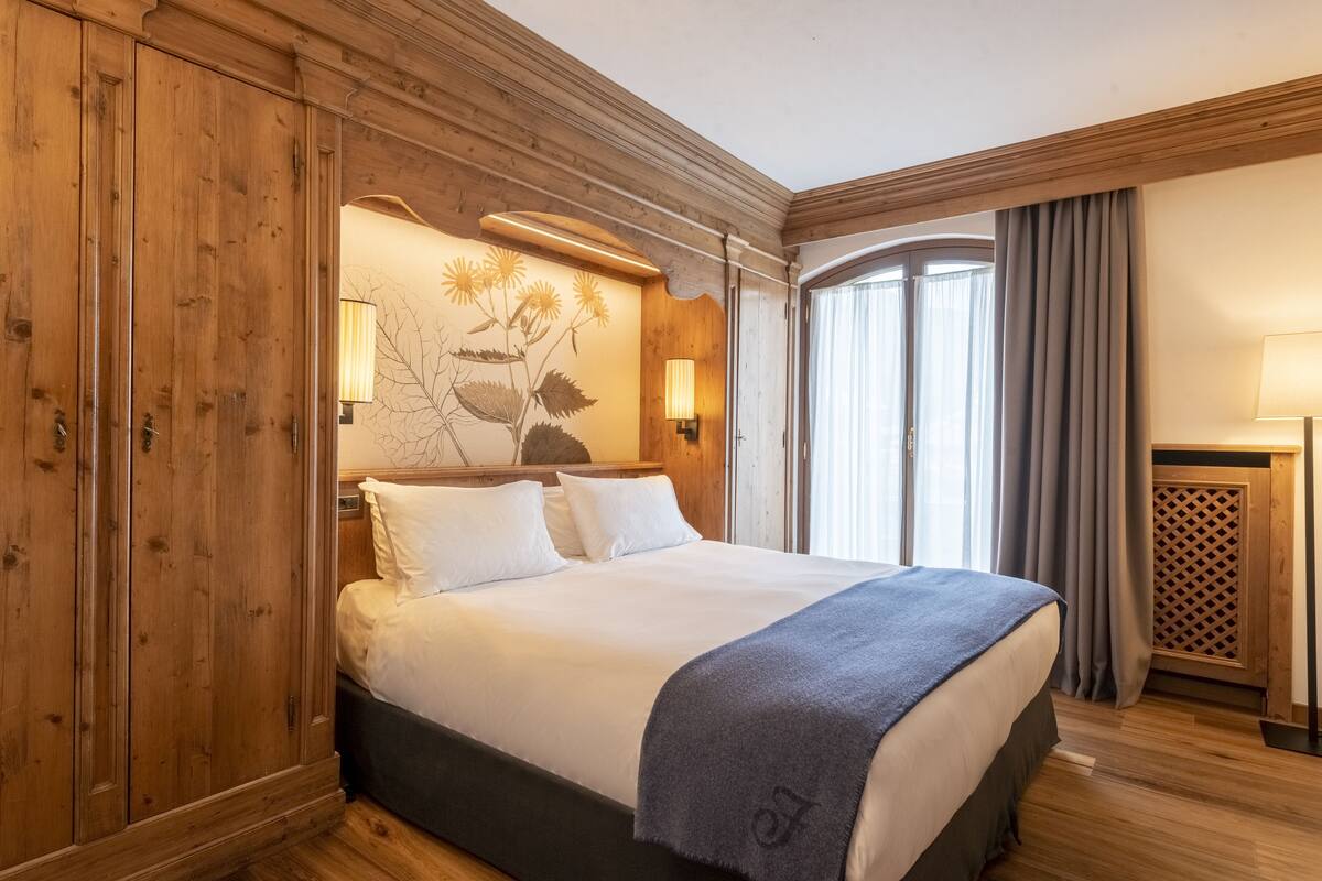 A hotel room with a wooden headboard, a large bed with white linens, a decorative wall piece, and a window with curtains.