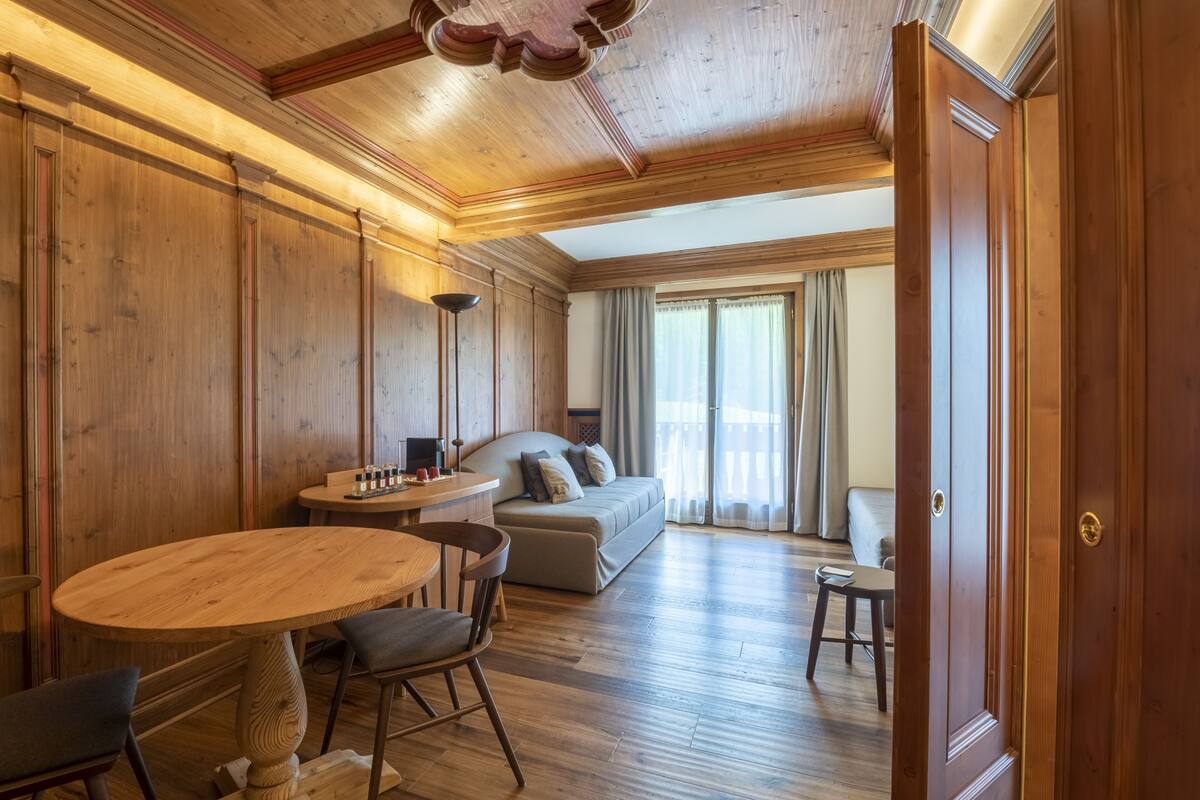 A wooden-paneled room with a round wooden table, two chairs, a sofa, and a small table with bottles.
