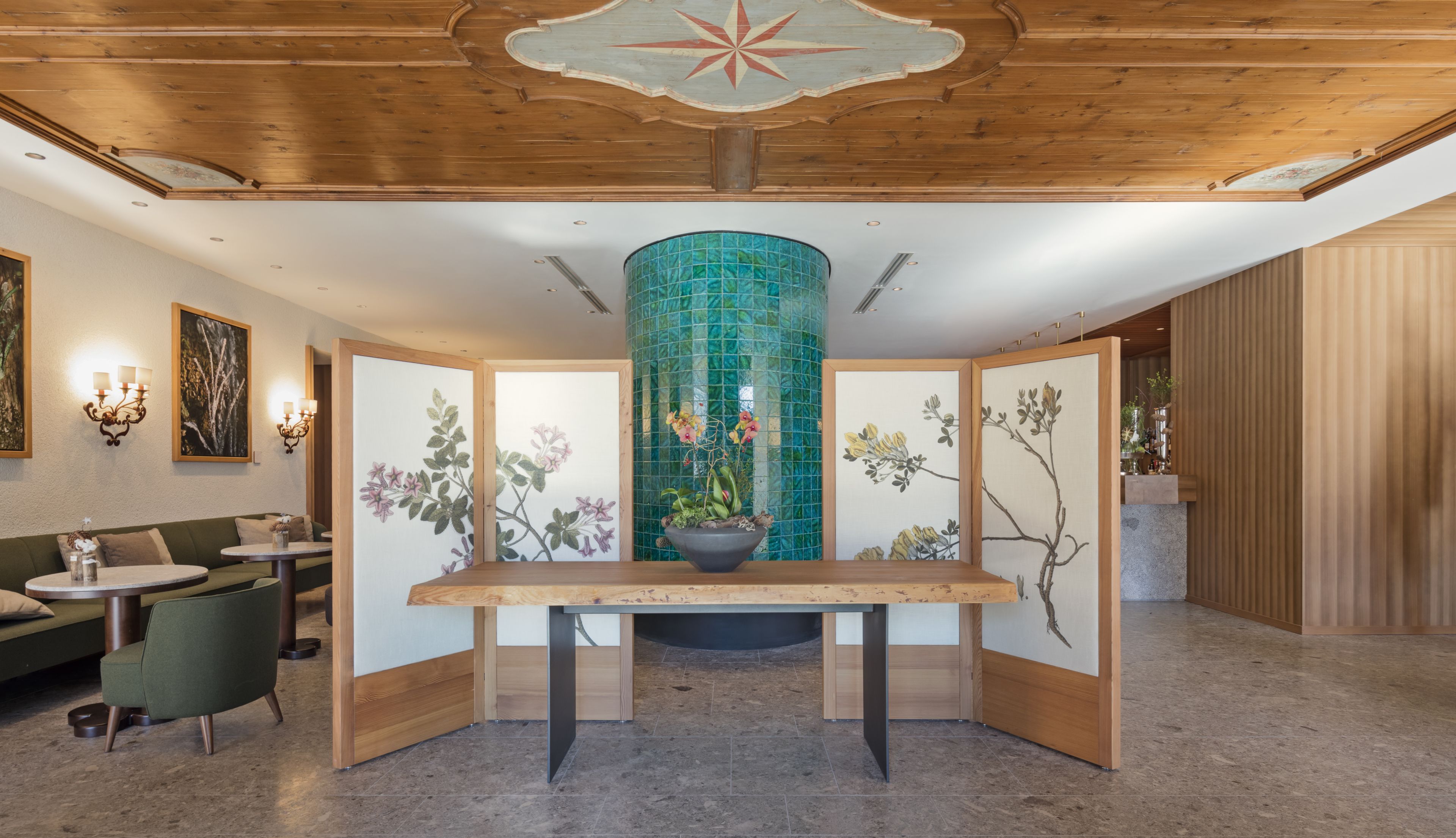 Una zona de recepción con techo de madera, una columna con azulejos verdes, un mostrador de recepción de madera y un sofá verde.