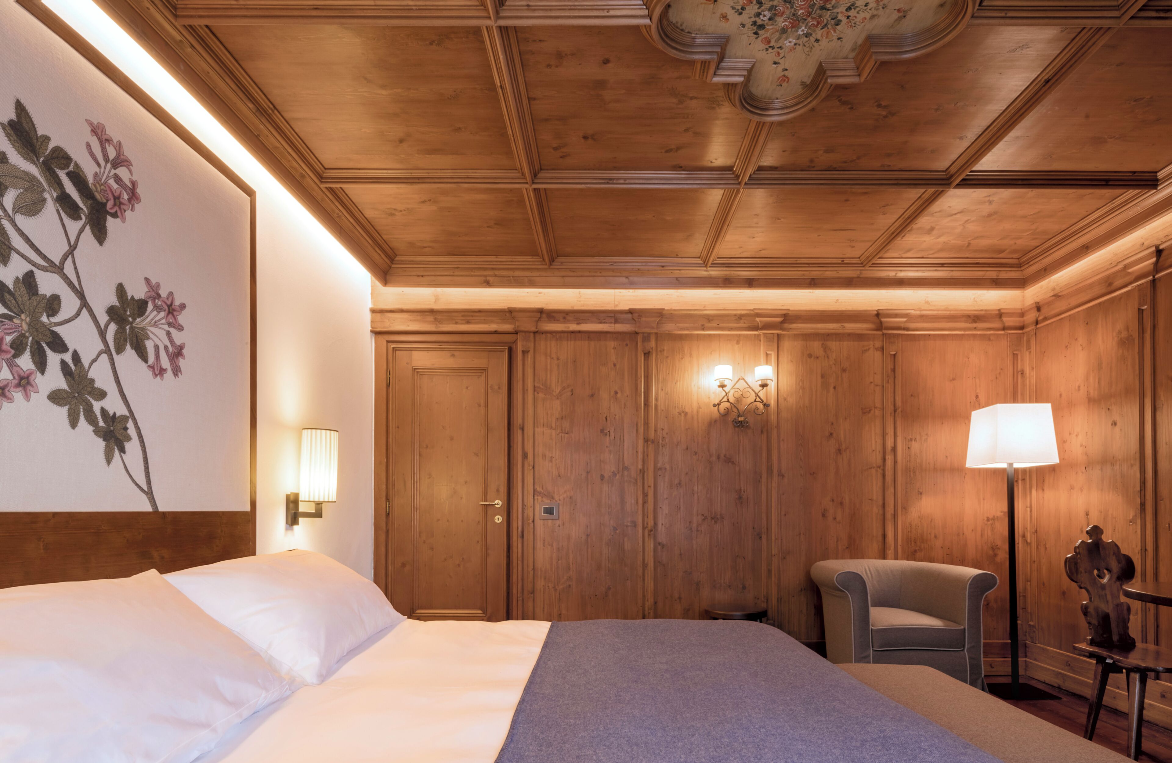 A hotel room with a bed, a chair, a lamp, and wooden paneling.