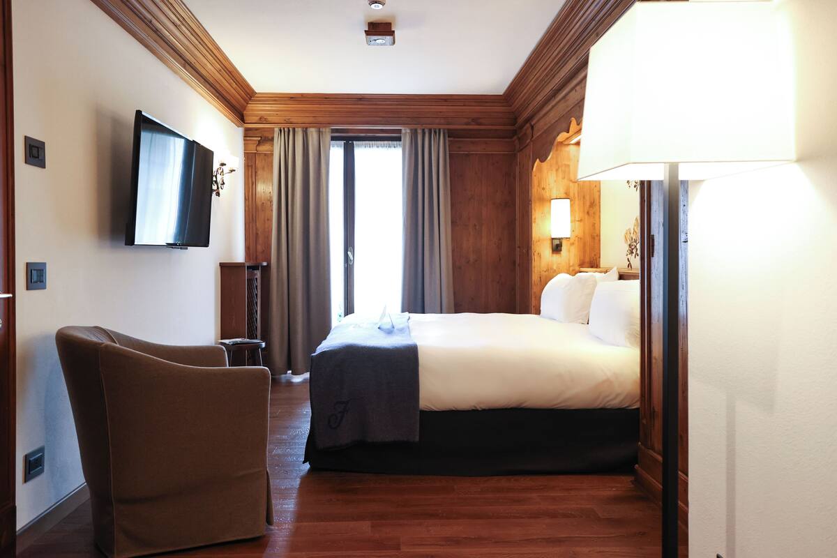 A hotel room with a bed, a chair, a TV, and a lamp.