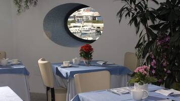 A dining area with round tables, chairs, and a view of boats through a circular window.