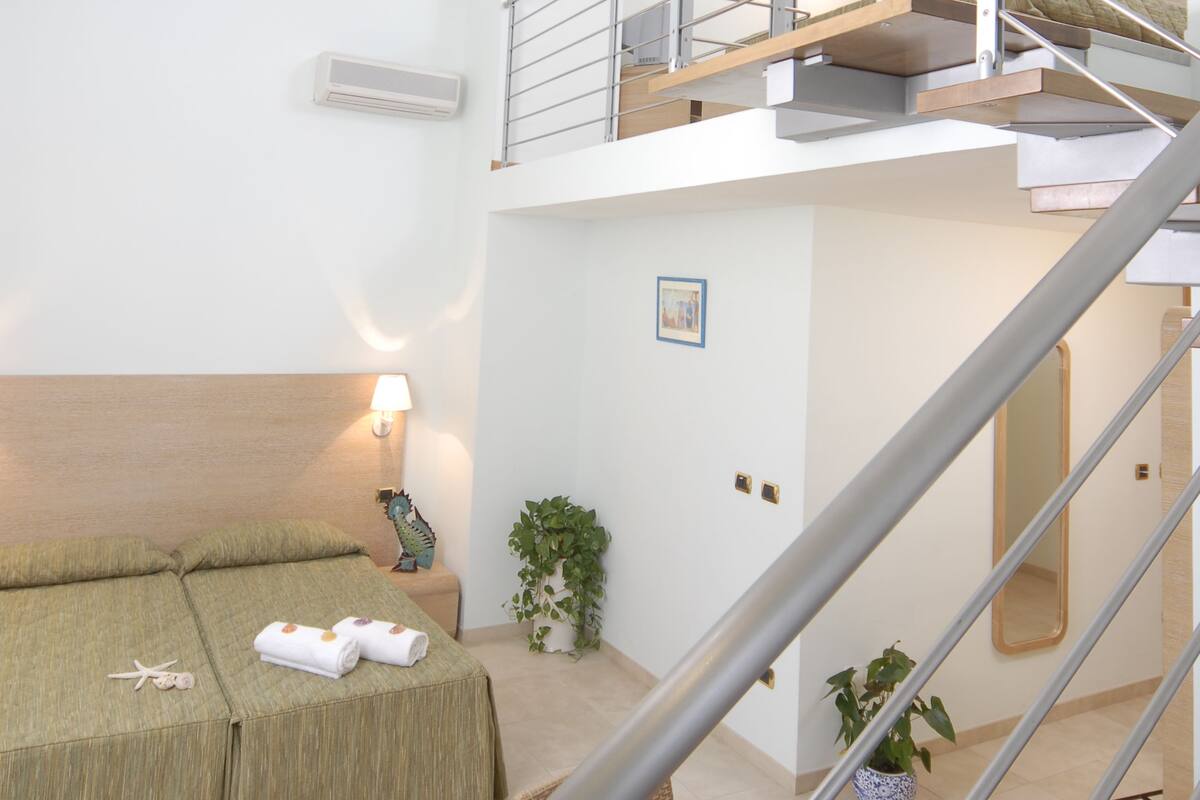 Un intérieur moderne avec un escalier, un canapé agrémenté de serviettes, une petite table avec des fruits et une plante en pot.