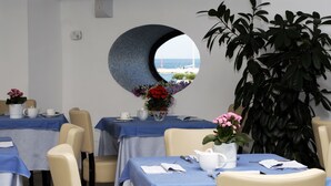Un comedor con mesas redondas, sillas y una planta grande en maceta.