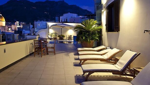 Terraza en la azotea con sillones de descanso y zona de comedor, con vistas a un paisaje urbano y montañas.