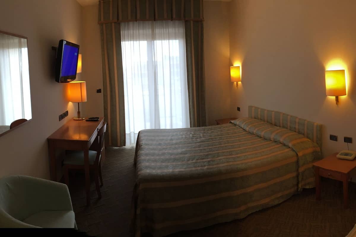 A hotel room with two beds, a desk, a chair, and a TV.