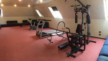 Un gimnasio con equipo de ejercicio, cinta de correr y piso cubierto de alfombra roja.