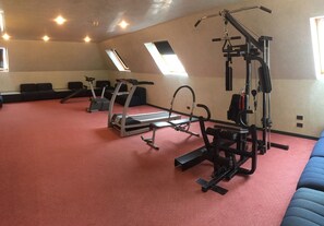 Une salle de sport équipée de matériel d’exercice, d’un tapis de course et dotée d’un sol recouvert d’une moquette rouge.