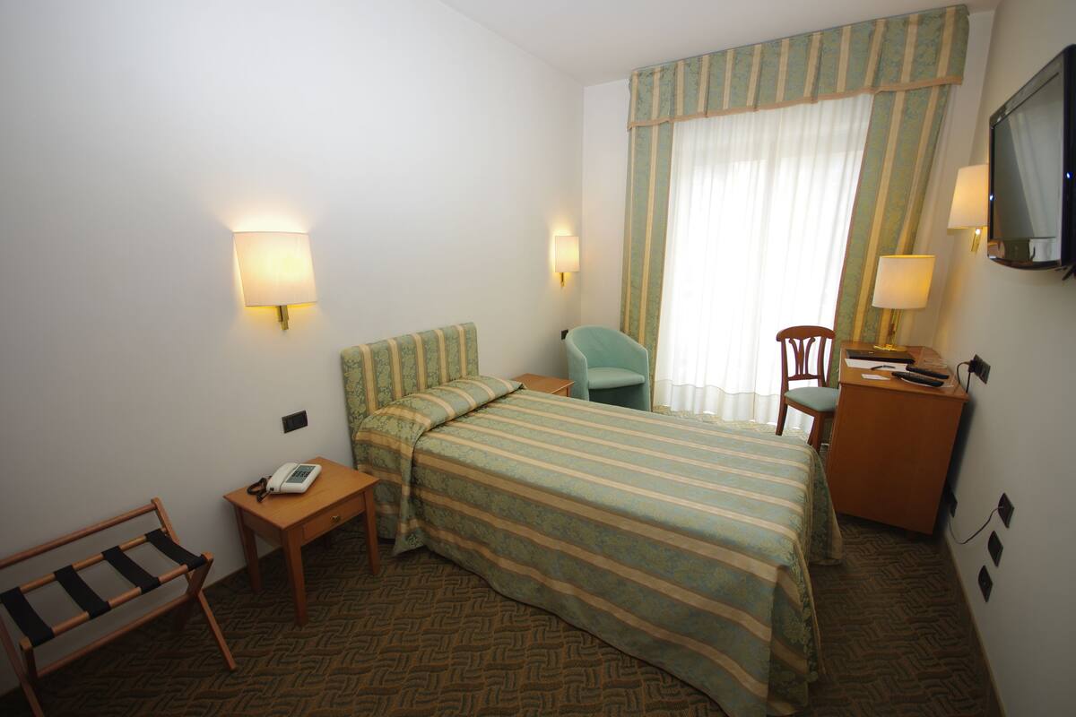 A hotel room with a bed, two chairs, a desk, a telephone, and a television.