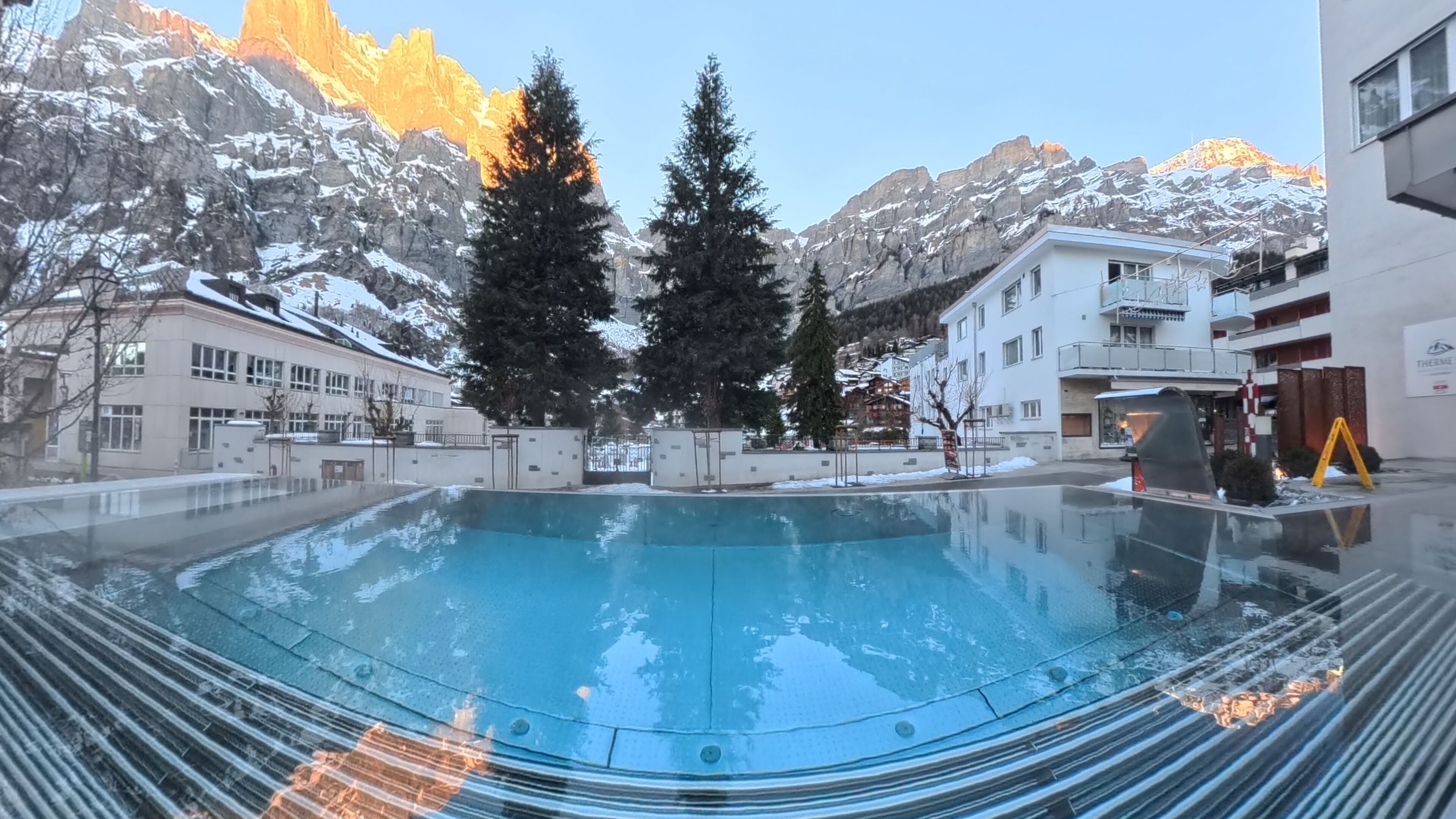 A swimming pool with a mountain backdrop, surrounded by buildings and trees.