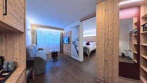 A modern hotel room with a wooden interior, a sofa, a small table, a bed, and a TV.