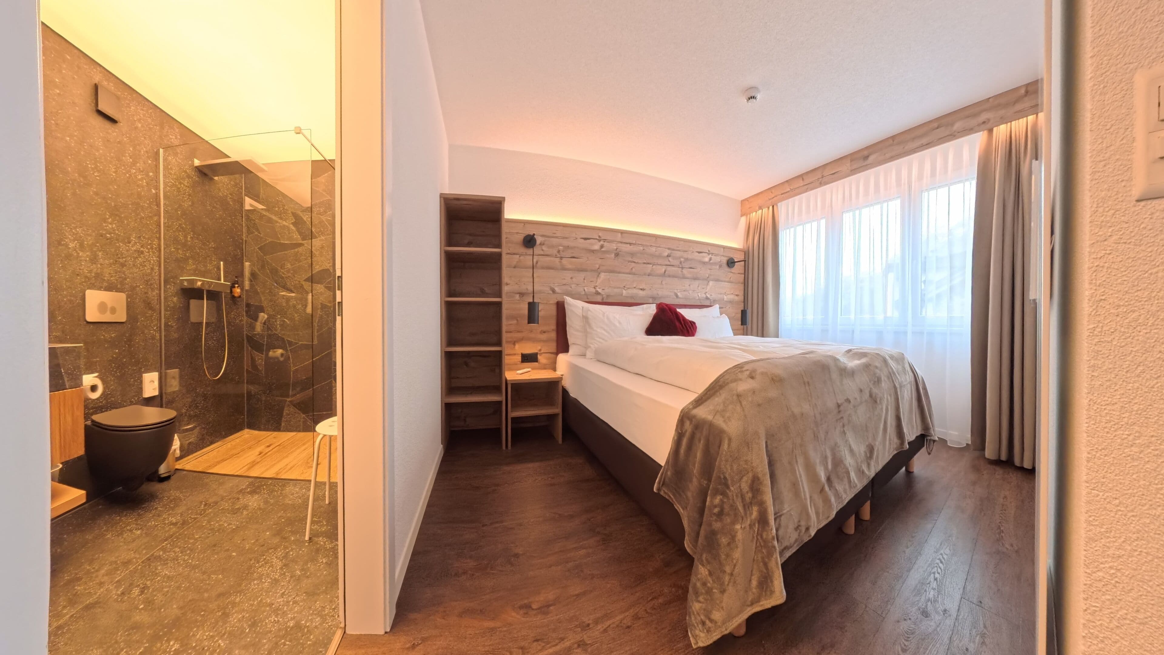 A modern hotel room with a shower, a bed, a nightstand, and a wooden headboard.