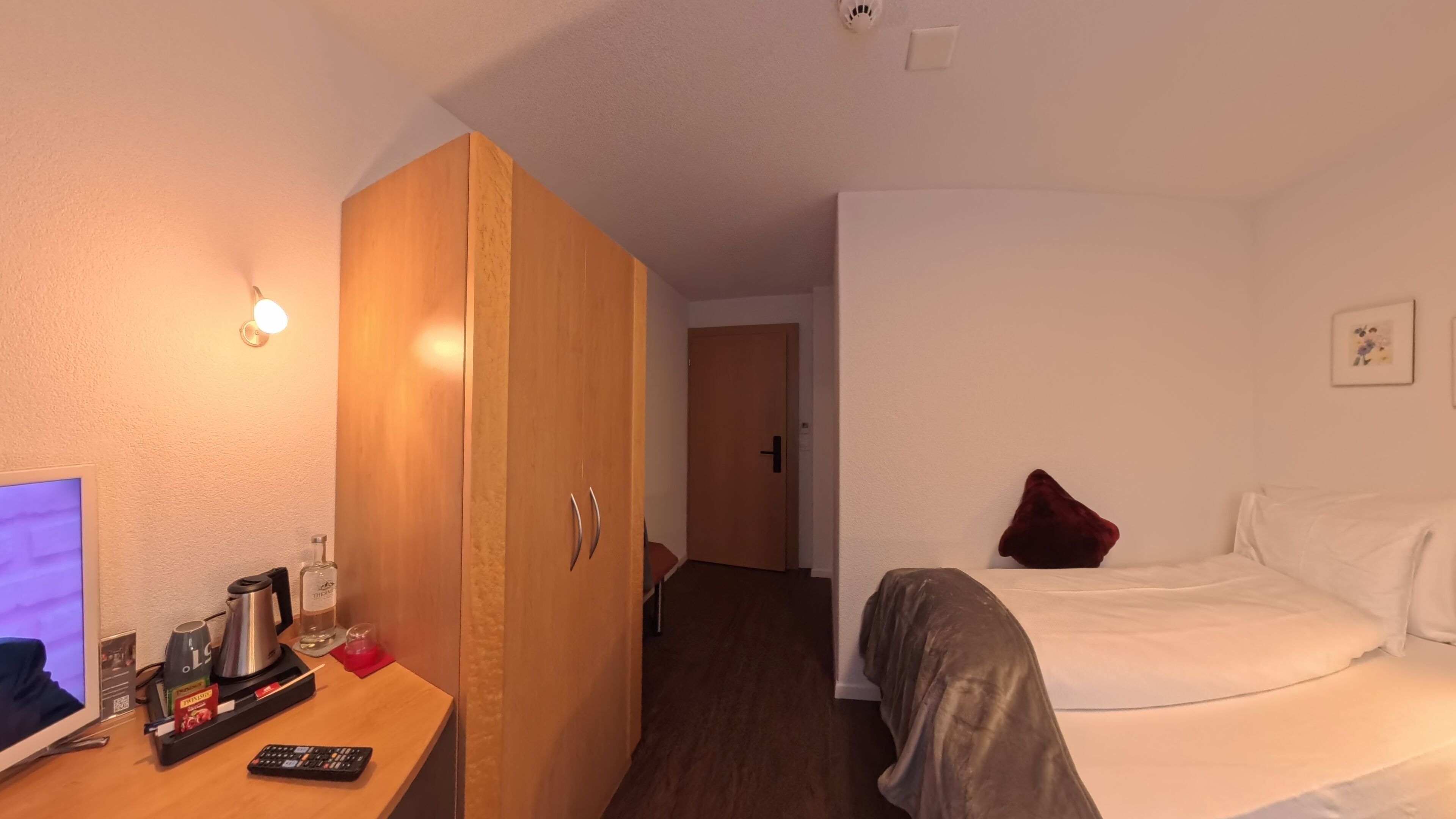 Ein Hotelzimmer mit einem Bett, einem Schreibtisch mit Fernseher, einem Kleiderschrank und einer Tür zu einem weiteren Raum.