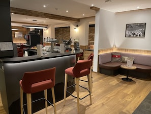 A modern bar area with a counter, stools, and a seating area with a checkered sofa and a small table.