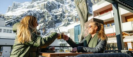 Two people toasting at a table with a mountain view in the background.