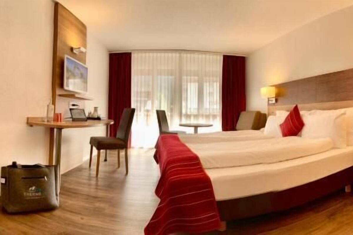 A hotel room with a bed, a desk, a chair, and a small table.