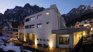 A modern hotel with a terrace, large windows, and a view of snow-capped mountains.