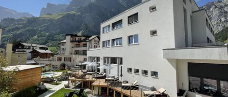 Un hotel moderno con zona de piscina, mobiliario exterior y vistas a las montañas.