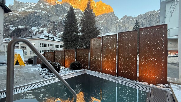 A pool area with a metal staircase leading into the water, surrounded by metal panels with holes, and a mountain backdrop.
