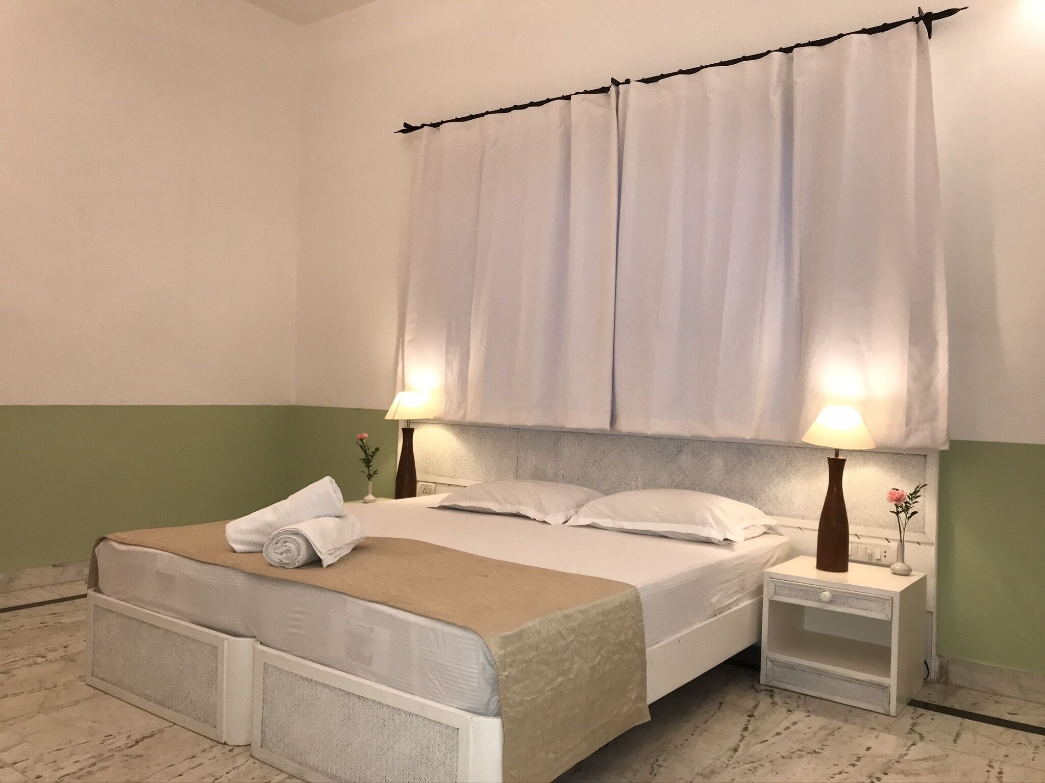 A hotel room with a bed, two bedside tables, a nightstand, a lamp, and a vase with a flower.