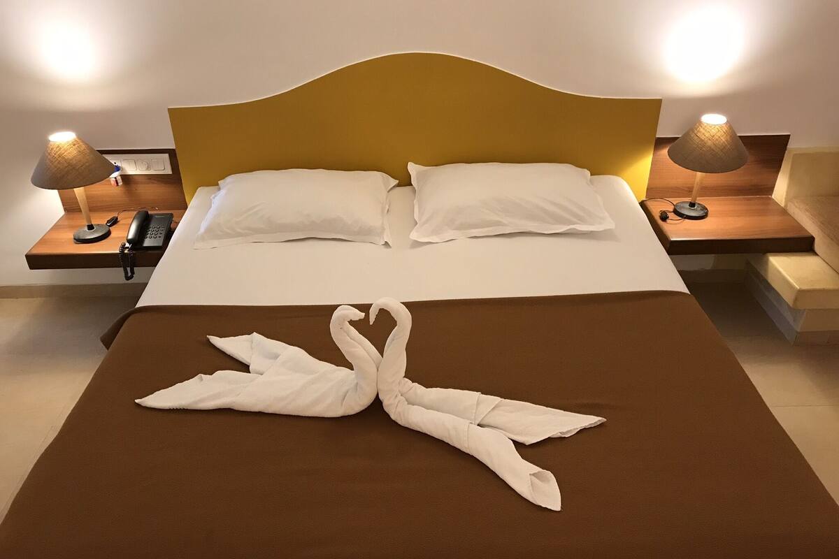 Habitación de hotel con cama, dos lámparas de noche, un teléfono y una escultura de toalla en la cama.