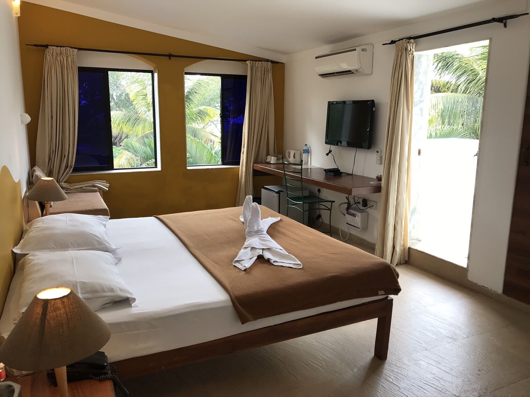Une chambre d’hôtel avec un lit, un bureau, une télévision et une fenêtre avec des rideaux.