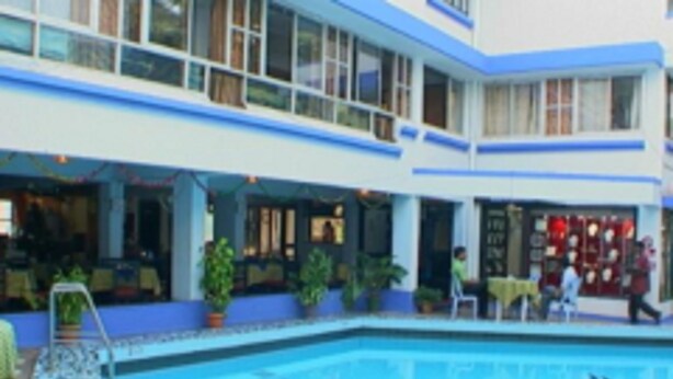 Una piscina interior con vista despejada al área de la piscina, un área de descanso con asientos y un restaurante con comensales.