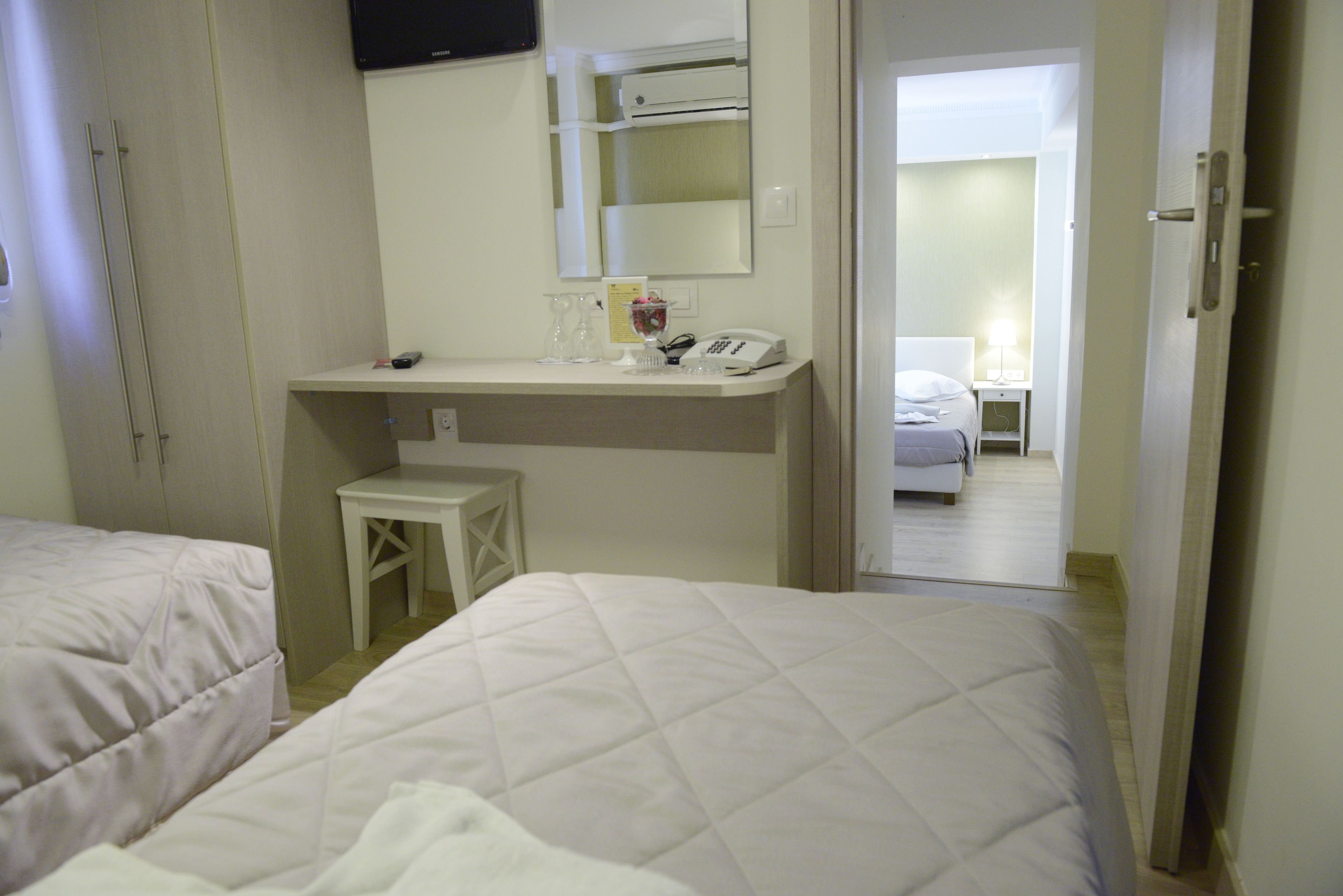 A hotel room with two beds, a desk with a telephone, a small stool, and a mirror.