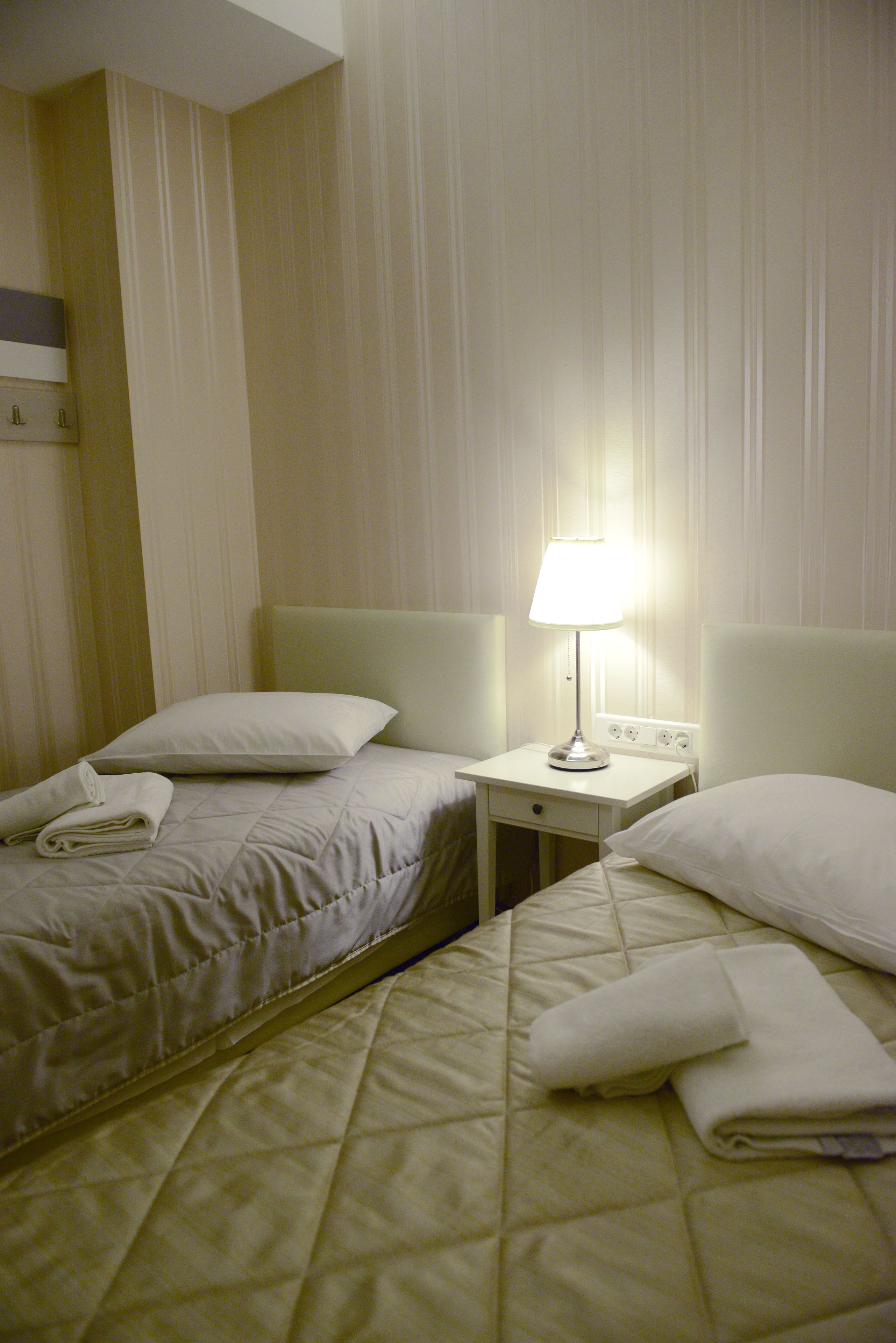 A hotel room with two beds, a nightstand, and a lamp.