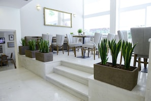 A modern interior with a staircase leading to a dining area, featuring grey chairs, a table, and potted plants. - Phidias Hotel by Oniro (Athens)