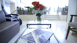 Un salon moderne avec une table basse en verre sur laquelle est posé un livre intitulé « L’envie prend le dessus ». Un vase contenant des fleurs rouges et blanches se trouve sur la table.